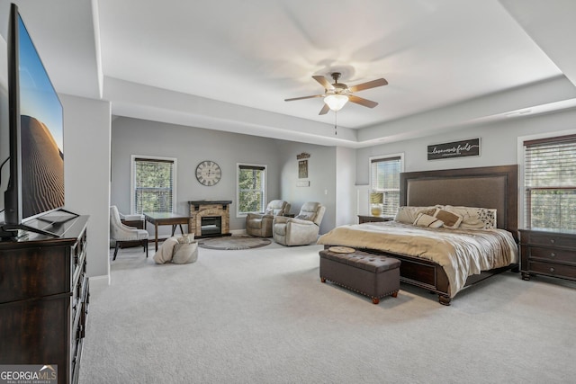 bedroom featuring ceiling fan, a fireplace, light carpet, and multiple windows