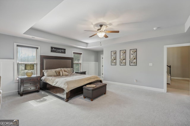 carpeted bedroom with ceiling fan and a raised ceiling