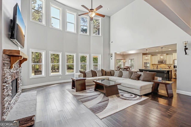 living room with ceiling fan, dark hardwood / wood-style flooring, a towering ceiling, and a fireplace