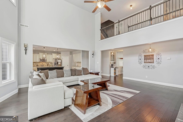 living room with ceiling fan, dark wood-type flooring, and a high ceiling