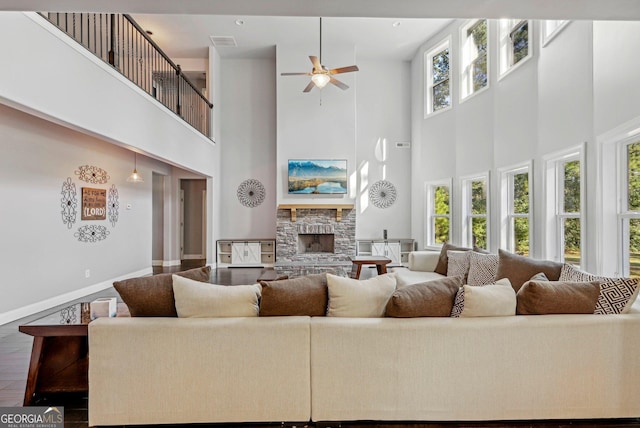 living room with a stone fireplace, a healthy amount of sunlight, a high ceiling, and wood-type flooring