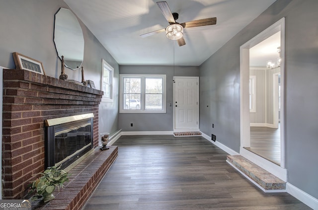 unfurnished living room with ceiling fan with notable chandelier, dark hardwood / wood-style floors, and a brick fireplace