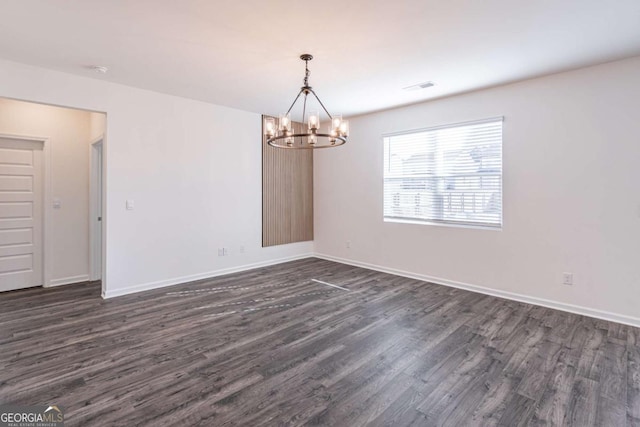 spare room featuring dark hardwood / wood-style flooring and a chandelier