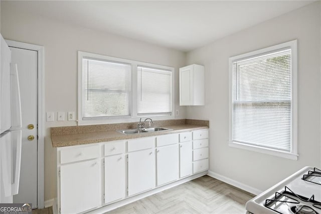 kitchen with stove, white cabinetry, a wealth of natural light, and sink