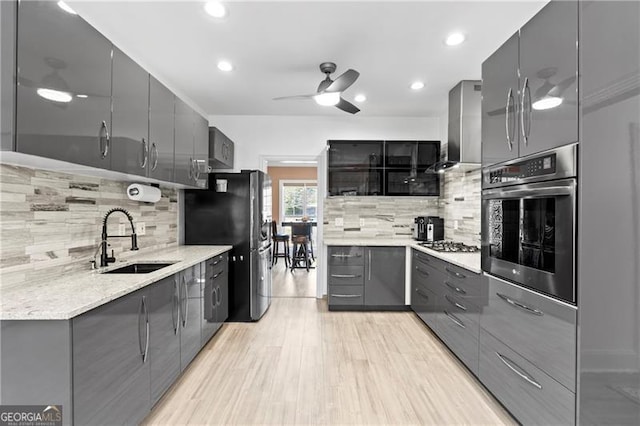 kitchen featuring decorative backsplash, appliances with stainless steel finishes, light wood-type flooring, sink, and wall chimney range hood