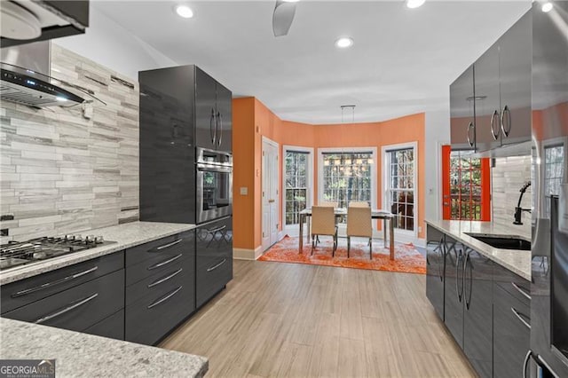 kitchen with hanging light fixtures, light hardwood / wood-style floors, backsplash, and appliances with stainless steel finishes