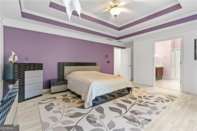 bedroom featuring connected bathroom, ceiling fan, light hardwood / wood-style flooring, crown molding, and a tray ceiling