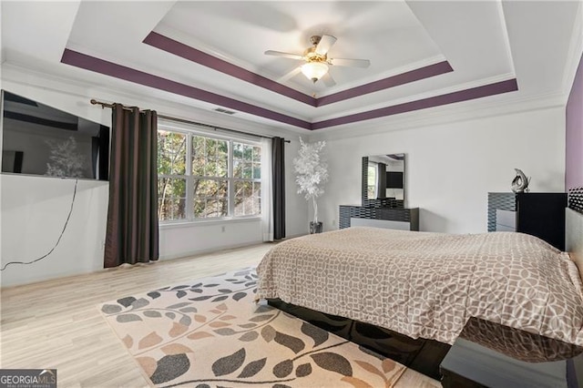 bedroom with wood-type flooring, a raised ceiling, ceiling fan, and ornamental molding