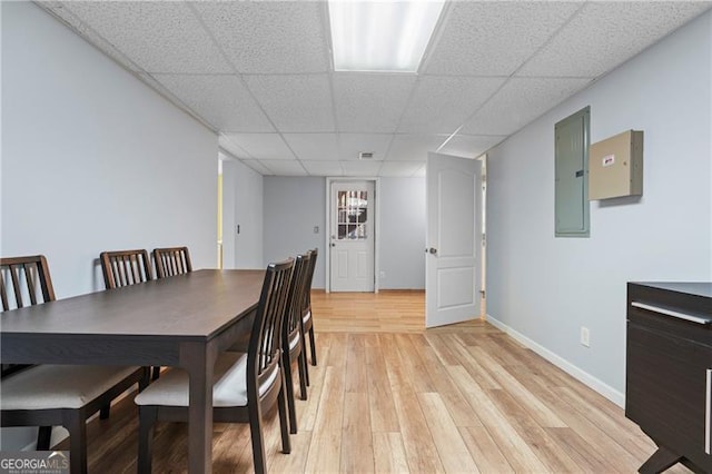 dining room featuring a paneled ceiling, light hardwood / wood-style flooring, and electric panel