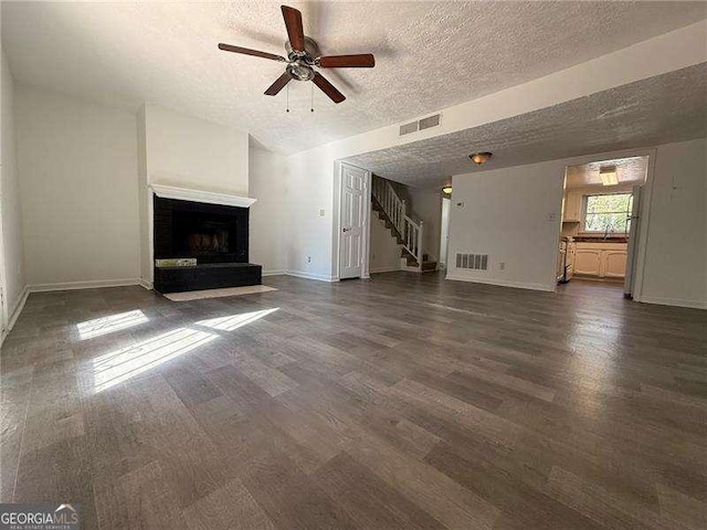 unfurnished living room featuring a textured ceiling, dark hardwood / wood-style floors, a brick fireplace, and ceiling fan