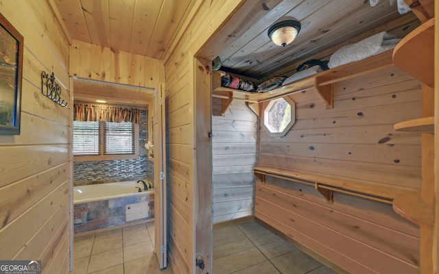 bathroom featuring tile patterned flooring, a relaxing tiled tub, and wood walls