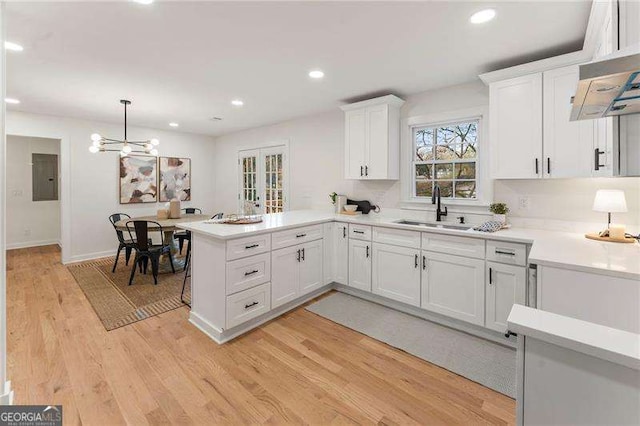 kitchen with white cabinets, kitchen peninsula, sink, and light hardwood / wood-style flooring