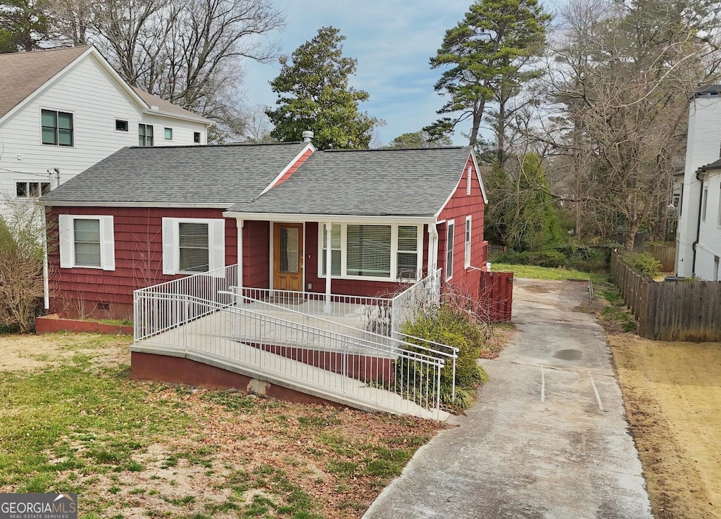 view of front of house with a porch, crawl space, a shingled roof, and fence