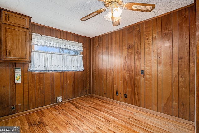 empty room featuring wood walls, light hardwood / wood-style flooring, and ceiling fan