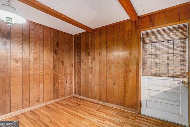 empty room featuring beam ceiling, light hardwood / wood-style flooring, and wooden walls