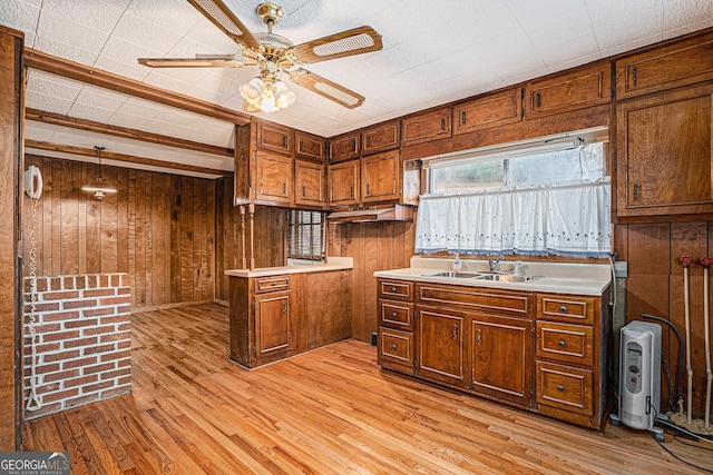 kitchen with kitchen peninsula, light wood-type flooring, ceiling fan, wooden walls, and sink