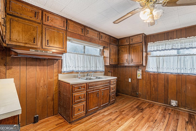 kitchen featuring wooden walls, sink, ceiling fan, and light hardwood / wood-style floors