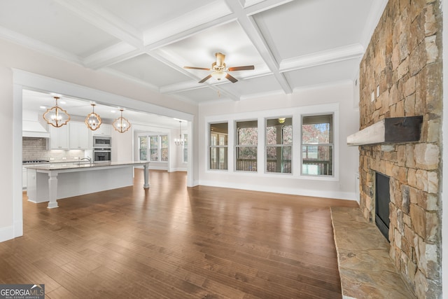 unfurnished living room with coffered ceiling, ceiling fan, beamed ceiling, a fireplace, and hardwood / wood-style floors