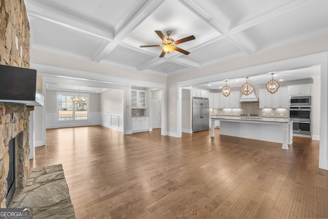 unfurnished living room featuring wood-type flooring, ceiling fan with notable chandelier, a stone fireplace, and beam ceiling