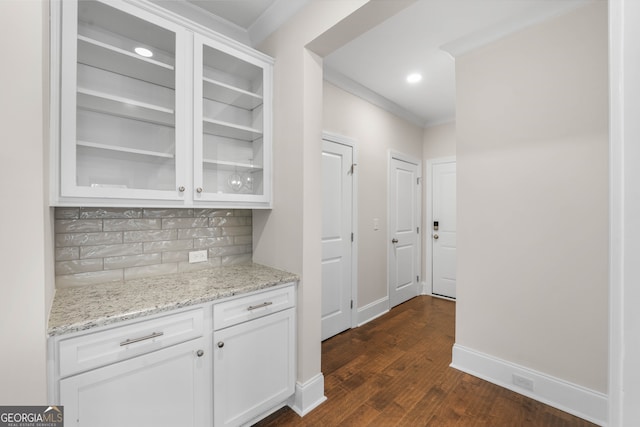 bar featuring light stone countertops, dark hardwood / wood-style flooring, tasteful backsplash, ornamental molding, and white cabinetry