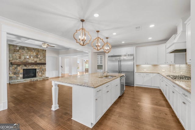 kitchen with white cabinetry, dark hardwood / wood-style flooring, an island with sink, pendant lighting, and a fireplace