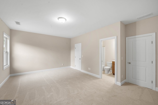 unfurnished bedroom with ensuite bathroom and light carpet