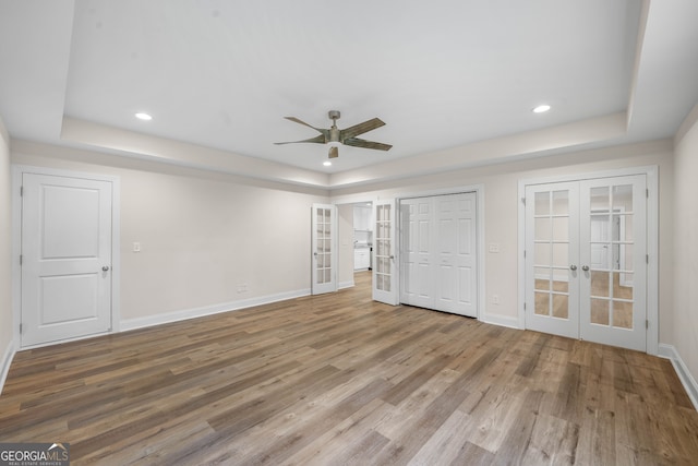 unfurnished bedroom with a raised ceiling, ceiling fan, french doors, and wood-type flooring