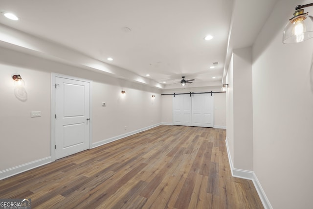 spare room featuring ceiling fan, a barn door, and wood-type flooring