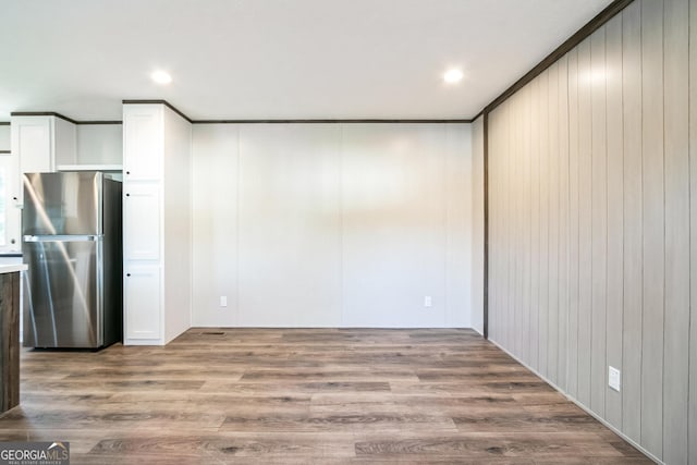 interior space with white cabinetry, stainless steel refrigerator, wooden walls, and light hardwood / wood-style flooring