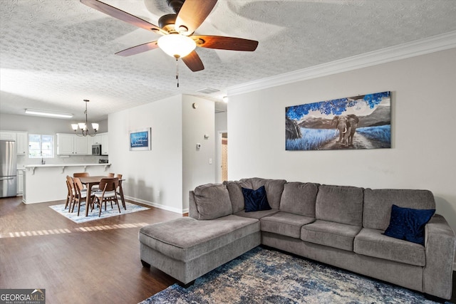 living room with ceiling fan with notable chandelier, dark hardwood / wood-style flooring, a textured ceiling, and ornamental molding