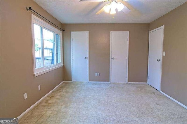 unfurnished bedroom featuring multiple closets, ceiling fan, light carpet, and a textured ceiling