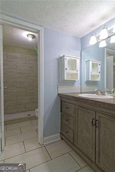 bathroom with a tile shower, vanity, a textured ceiling, and toilet