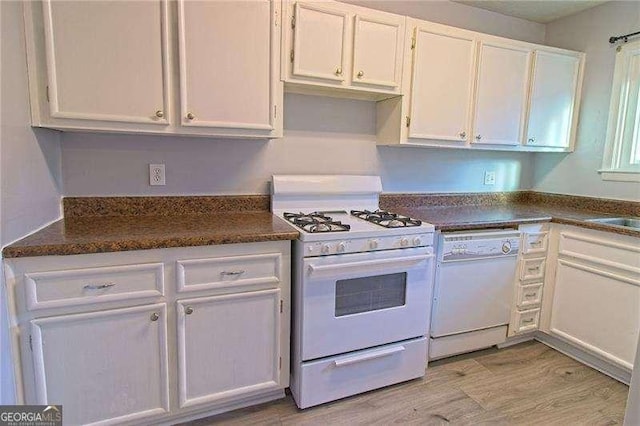 kitchen featuring white cabinetry, sink, dark stone countertops, white appliances, and light wood-type flooring