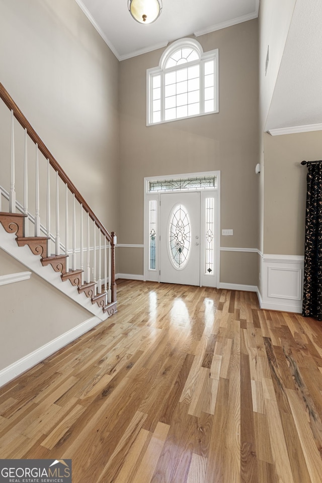 foyer with crown molding, light hardwood / wood-style floors, and a high ceiling