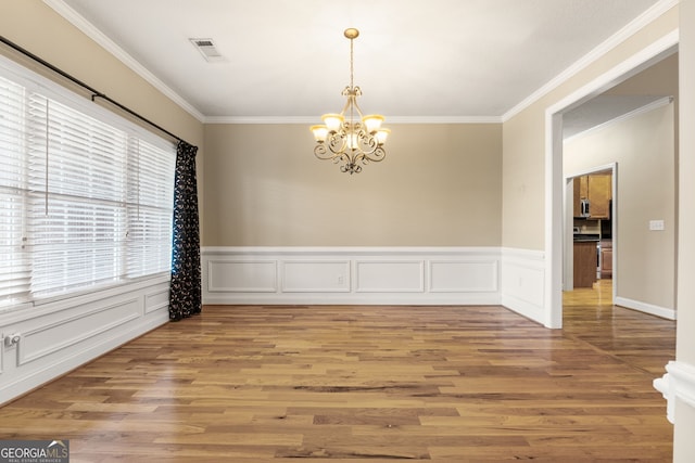 empty room featuring hardwood / wood-style flooring, ornamental molding, and an inviting chandelier