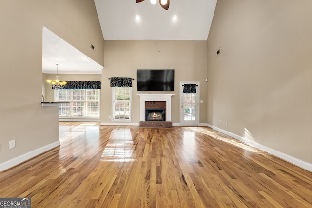 unfurnished living room featuring hardwood / wood-style floors, ceiling fan with notable chandelier, high vaulted ceiling, and a brick fireplace