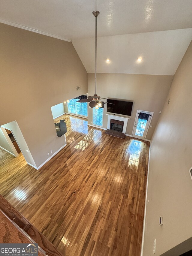 unfurnished living room with ceiling fan, high vaulted ceiling, and wood-type flooring