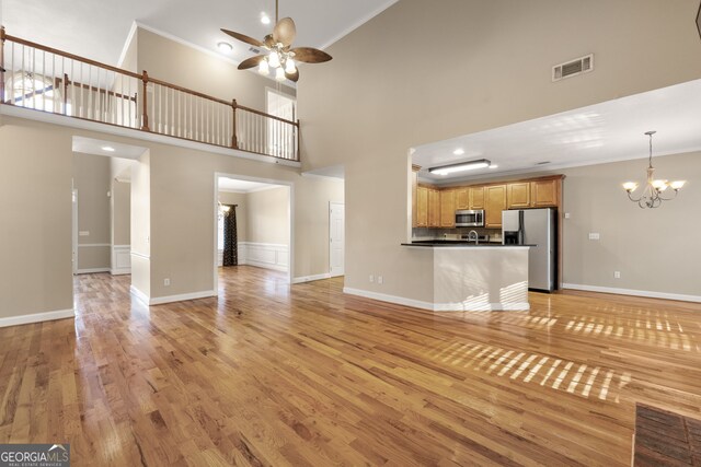 unfurnished living room featuring light hardwood / wood-style flooring, plenty of natural light, a towering ceiling, ceiling fan with notable chandelier, and ornamental molding