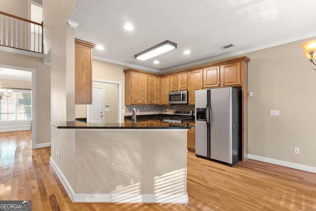 kitchen with dark stone counters, an inviting chandelier, light hardwood / wood-style flooring, kitchen peninsula, and stainless steel appliances