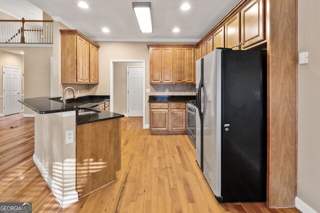 kitchen featuring sink, stainless steel appliances, kitchen peninsula, dark stone counters, and light hardwood / wood-style floors