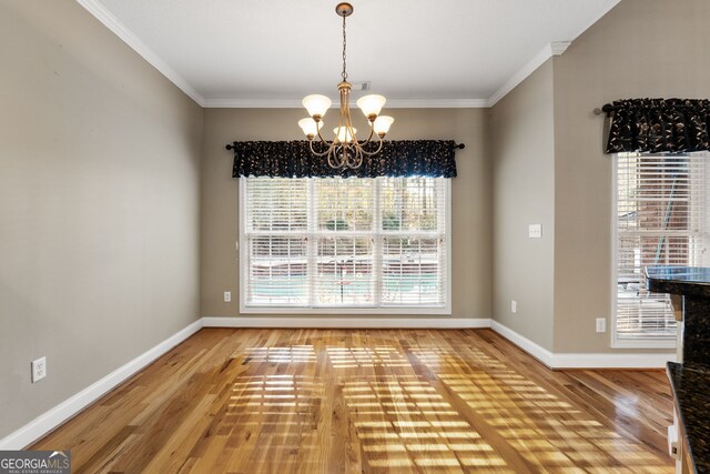 unfurnished dining area with wood-type flooring, ornamental molding, and a chandelier