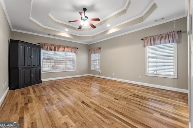 empty room with ceiling fan, a raised ceiling, light wood-type flooring, and ornamental molding