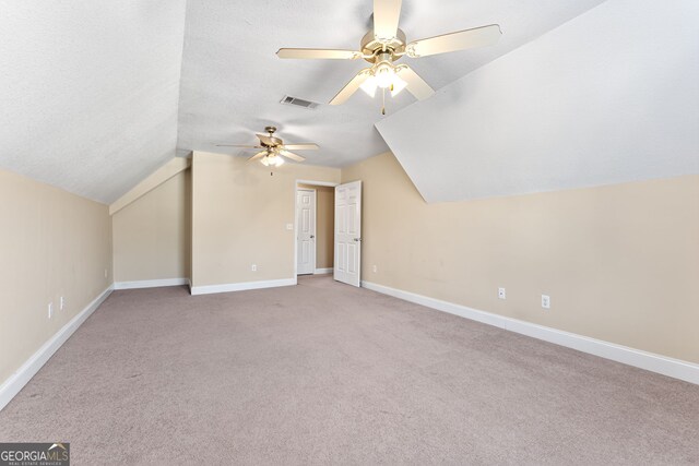 bonus room with a textured ceiling, light colored carpet, vaulted ceiling, and ceiling fan