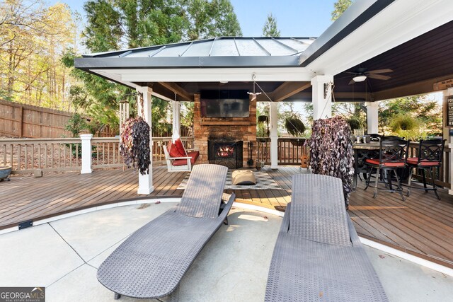 view of patio / terrace with a gazebo, ceiling fan, an outdoor stone fireplace, and a deck