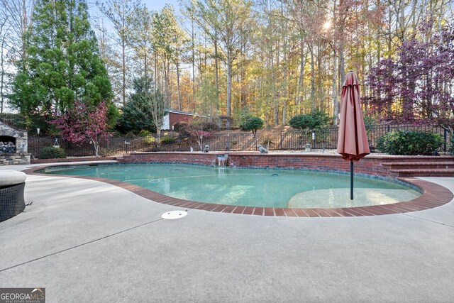 view of pool featuring pool water feature, an outdoor stone fireplace, and a patio