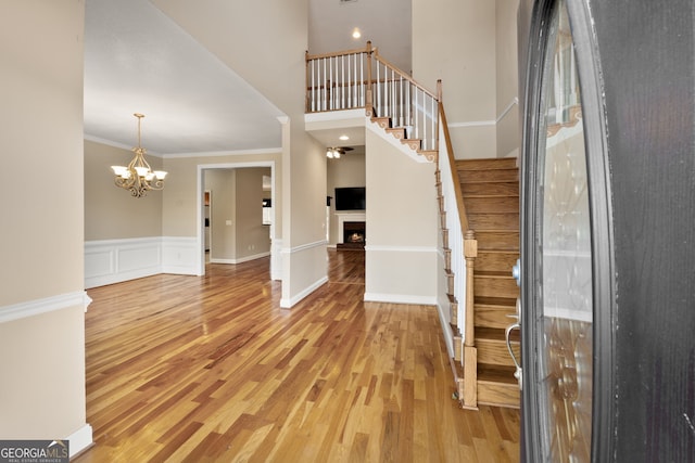 entryway with crown molding, hardwood / wood-style floors, a towering ceiling, and a notable chandelier