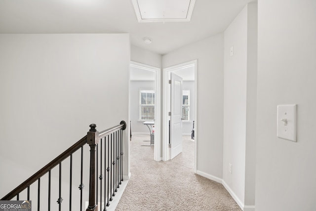 corridor with baseboards, an upstairs landing, attic access, and light colored carpet