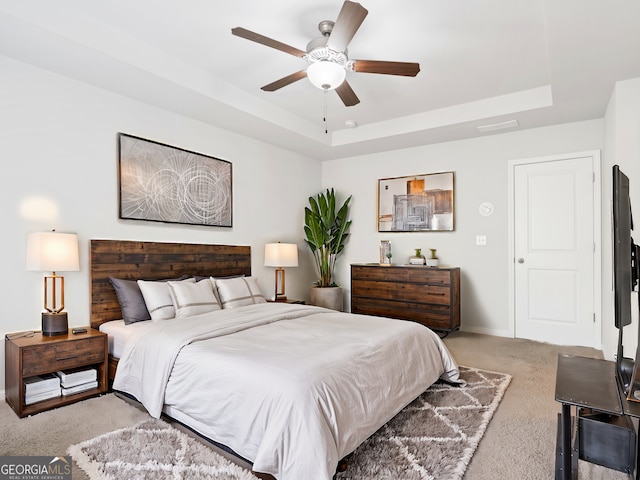 bedroom with light carpet, ceiling fan, a tray ceiling, and baseboards