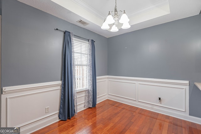 spare room featuring a raised ceiling, wood-type flooring, ornamental molding, and a chandelier