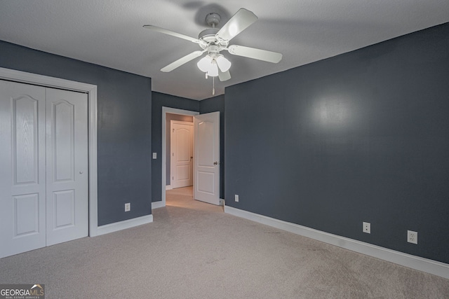 unfurnished bedroom featuring ceiling fan, light colored carpet, a textured ceiling, and a closet